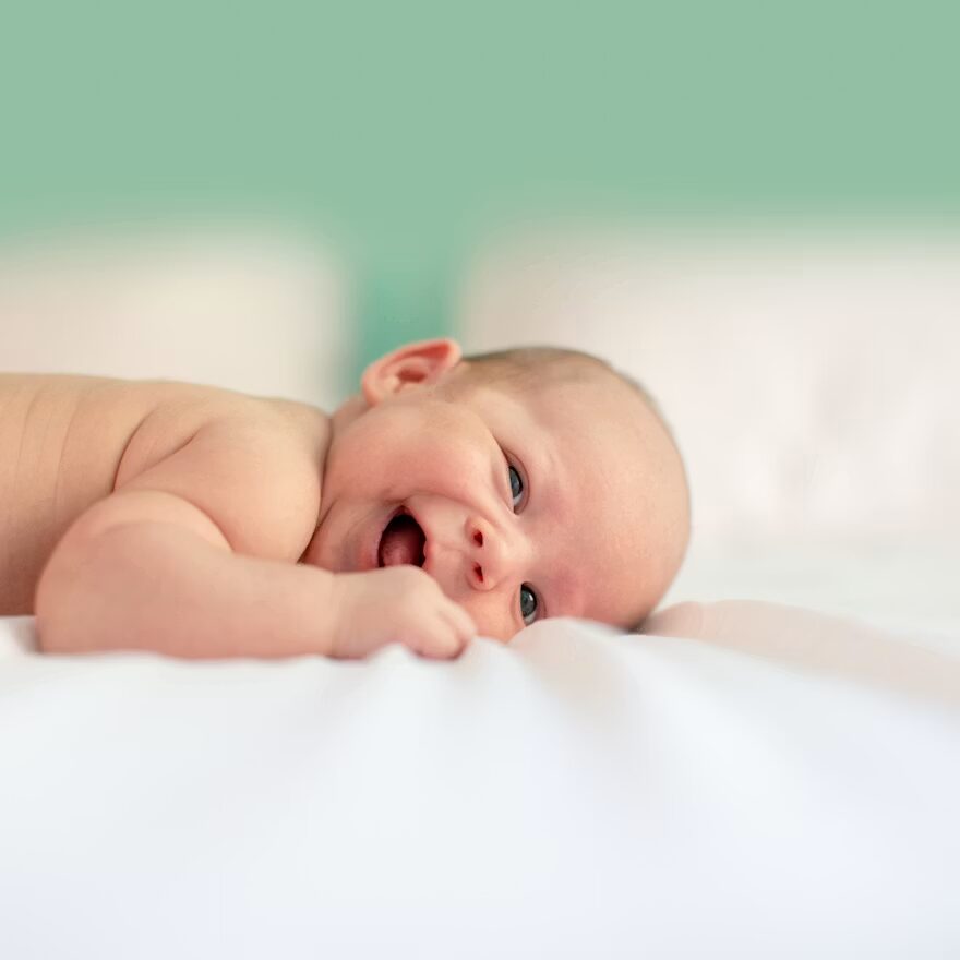Een baby ligt lachend op bed